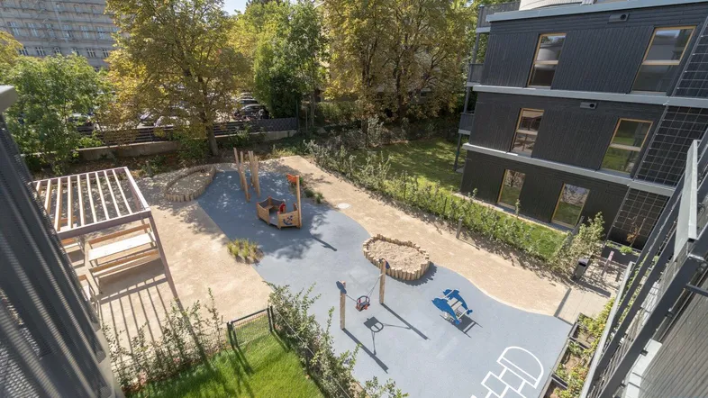 Moderner Spielplatz mit verschiedenen Spielgeräten und Sandkasten zwischen Wohngebäuden.
