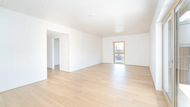 Helles, leeres Zimmer mit Holzboden und Zugang zu einem Außenbereich.