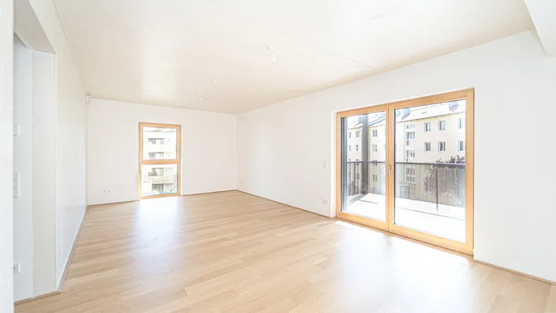 Helles Wohnzimmer mit Parkettboden und Zugang zu einem Balkon in einem Neubau.