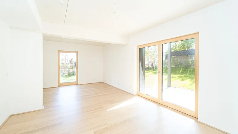 Helles Zimmer mit Holzboden und großen Schiebetüren, die zu einer Terrasse und dem Garten führen.