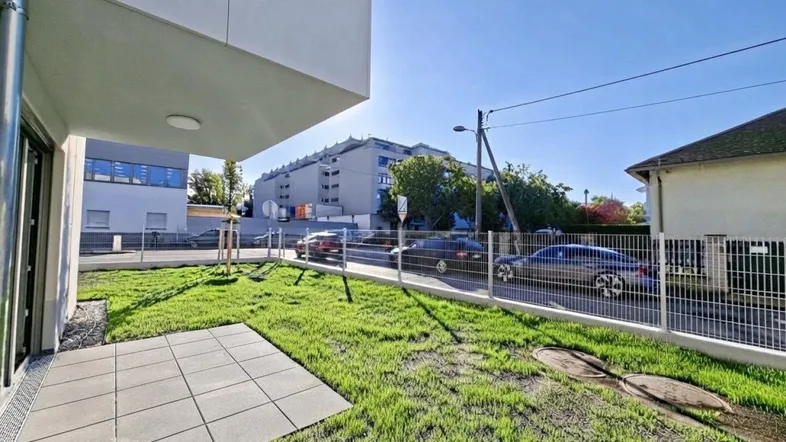 Moderne Gebäudefassade mit kleiner Terrasse und frischem Rasenbereich unter blauem Himmel.