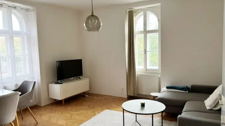 Helles Wohnzimmer mit Parkettboden, Sofa, Fernseher und einem kleinen Essbereich.