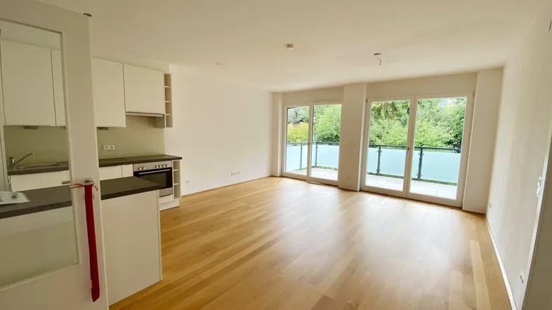 Heller Wohn- und Essbereich mit Parkettboden und Zugang zu einem Balkon mit Blick ins Grüne.