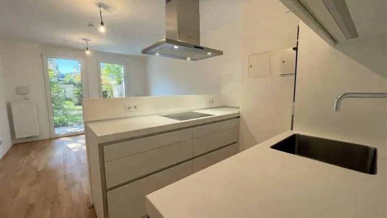 Moderne Küche mit heller Arbeitsplatte, Induktionskochfeld und direktem Zugang zum Garten.