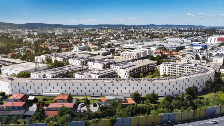 Luftaufnahme eines modernen, geschwungenen Wohnkomplexes mit vielen Balkonen in städtischer Umgebung.