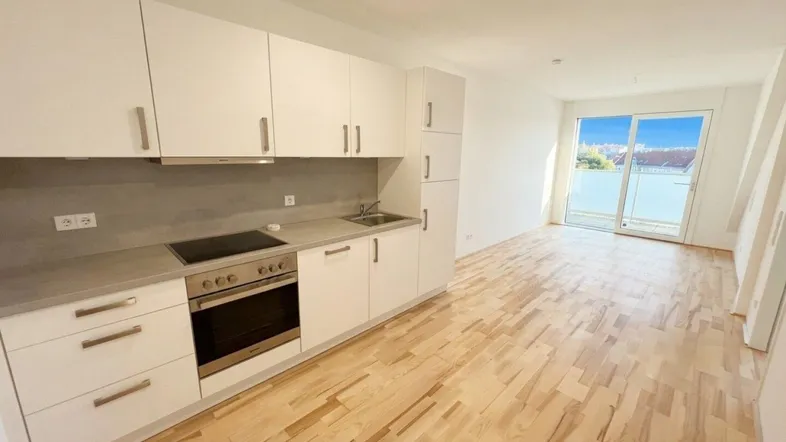 Helle, offene Wohnküche mit modernen weißen Schränken, Holzboden und Zugang zum Balkon.