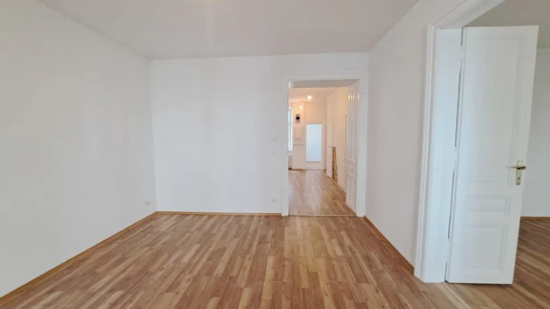 Helles, leeres Zimmer mit Laminatboden und weiß gestrichenen Wänden, bereit zur individuellen Gestaltung.