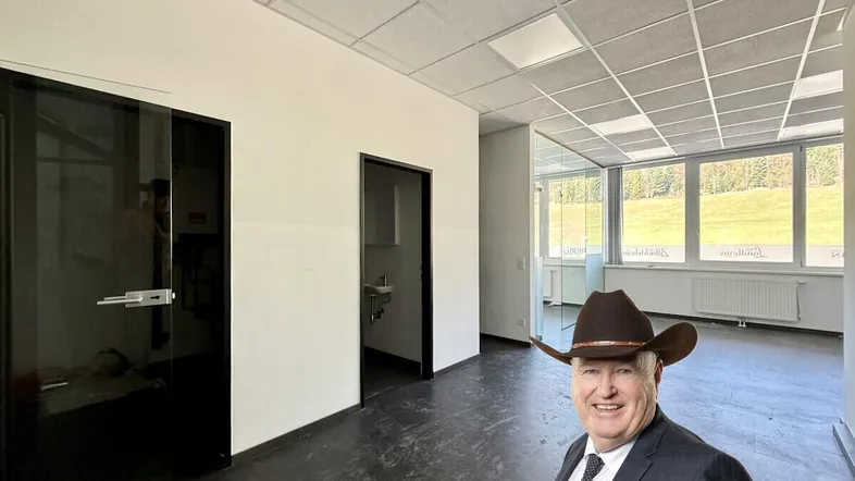 Geräumiges Büro mit dunklem Boden, weißen Wänden und großen Fenstern mit Blick auf die Landschaft und Berge.