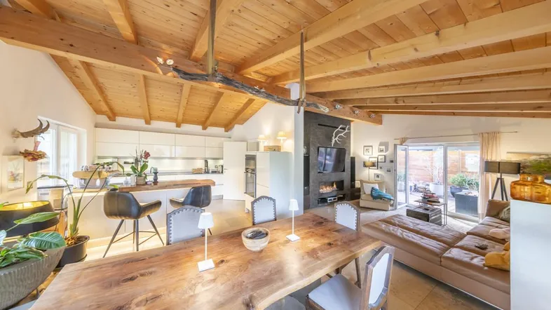 Geräumiger offener Wohn- und Essbereich mit Holzbalkendecke, moderner Küche und Zugang zur Terrasse.