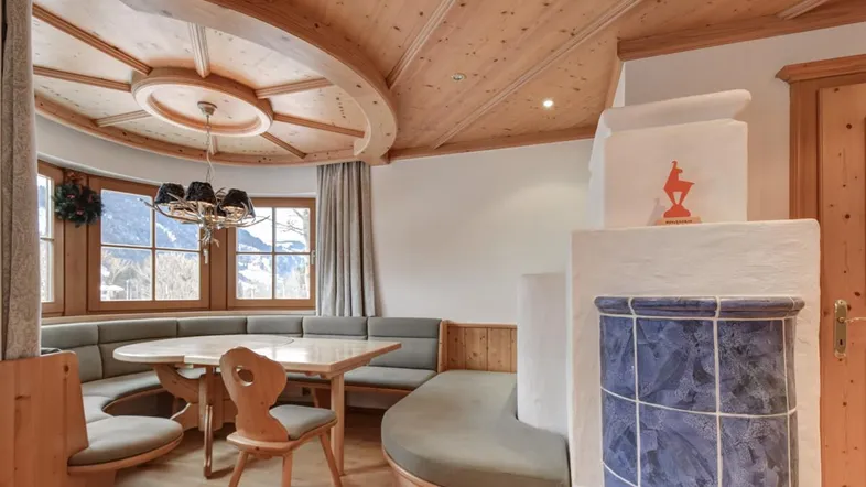 Gemütlicher Essbereich im alpinen Stil mit Holztäfelung, Eckbank und traditionellem Kachelofen.