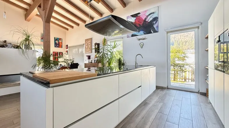Moderne Küche mit Kochinsel, Holzbalkendecke und Zugang zur Terrasse mit Bergblick.
