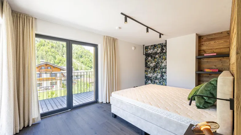 Helles Schlafzimmer mit Holzwand, floraler Tapete und Zugang zu einem Balkon mit Bergblick.