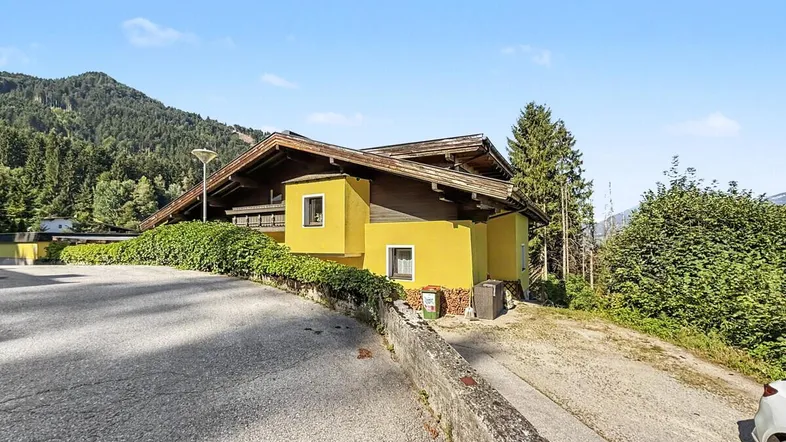 Gelbes Haus im alpinen Stil mit Holzelementen und umgebender Natur in sonniger Lage.