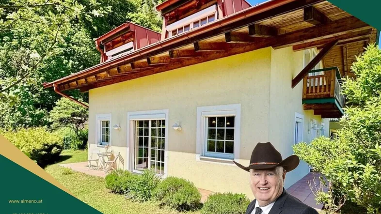 Hausfassade mit kleiner Terrasse und gepflegtem Garten in grüner Umgebung.