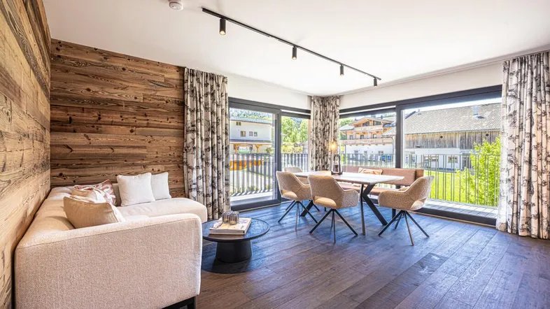 Heller Wohn- und Essbereich mit Holzwand, modernen Möbeln und Zugang zu einem Balkon.