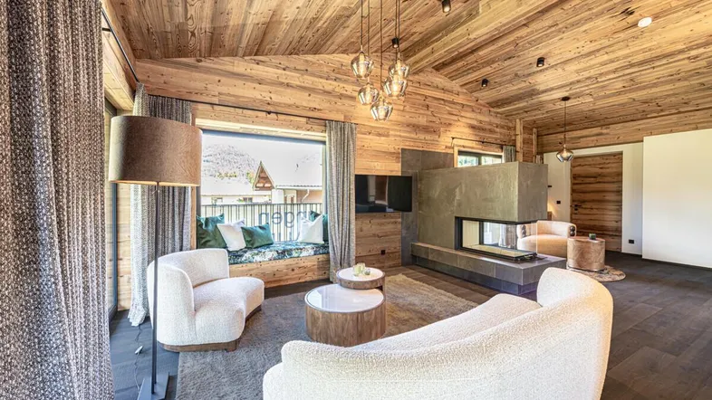 Gemütliches Wohnzimmer im alpinen Stil mit Kamin, Holzwänden und einem Fensterplatz mit Bergblick.