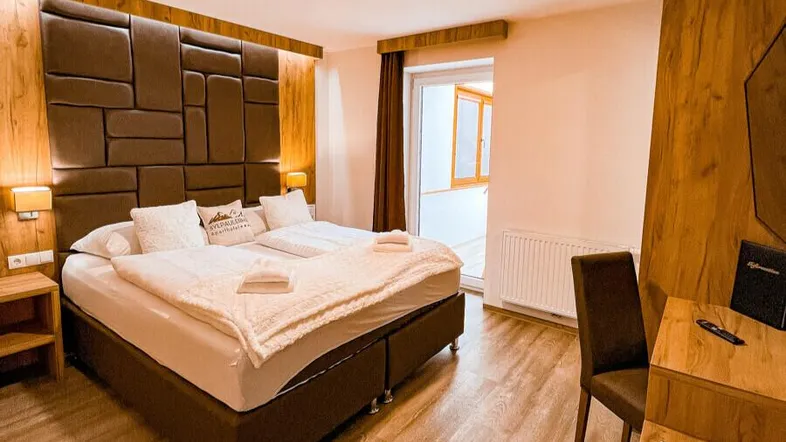 Gemütliches Schlafzimmer mit großem Doppelbett, Holzelementen und Zugang zu einem Balkon.