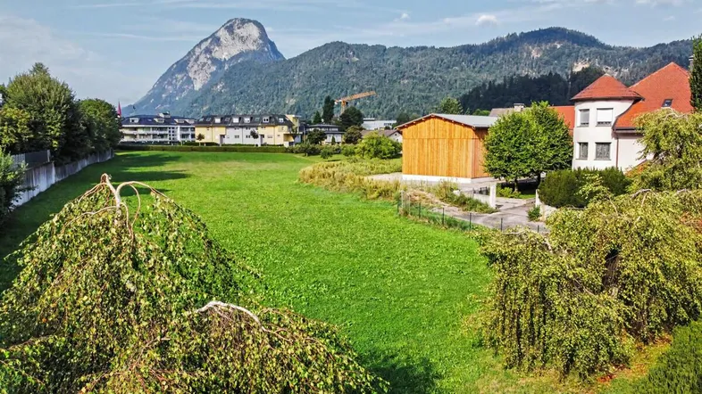 Weitläufige Grünfläche mit umliegenden Gebäuden und beeindruckendem Bergblick im Hintergrund.