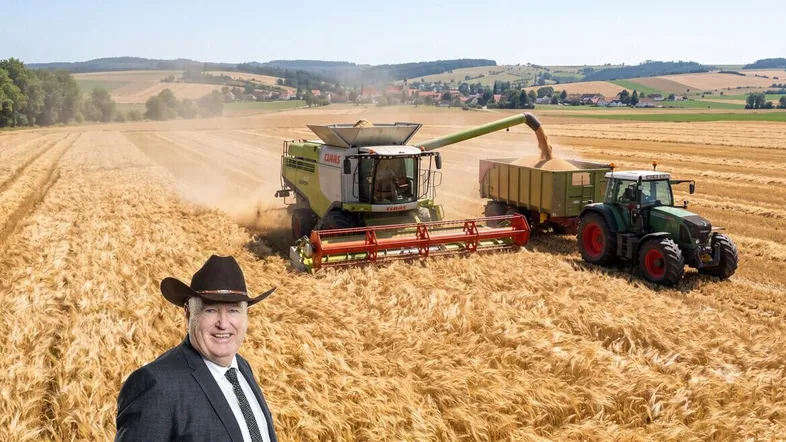 Mähdrescher und Traktor bei der Getreideernte auf einem weiten Feld mit ländlicher Umgebung.