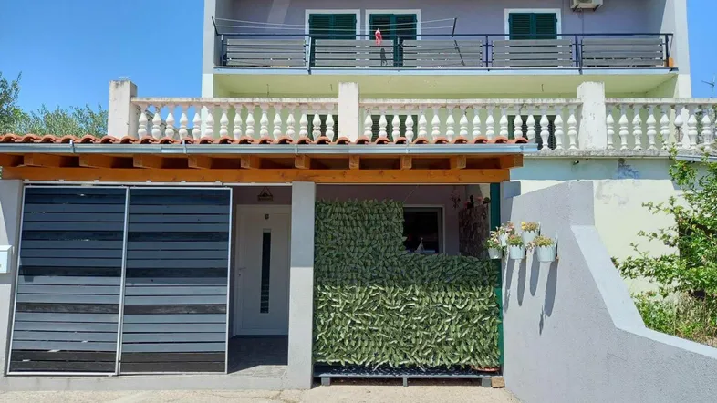 Fassade eines Wohnhauses mit Balkonen, überdachtem Eingangsbereich und Klimaanlage unter blauem Himmel.
