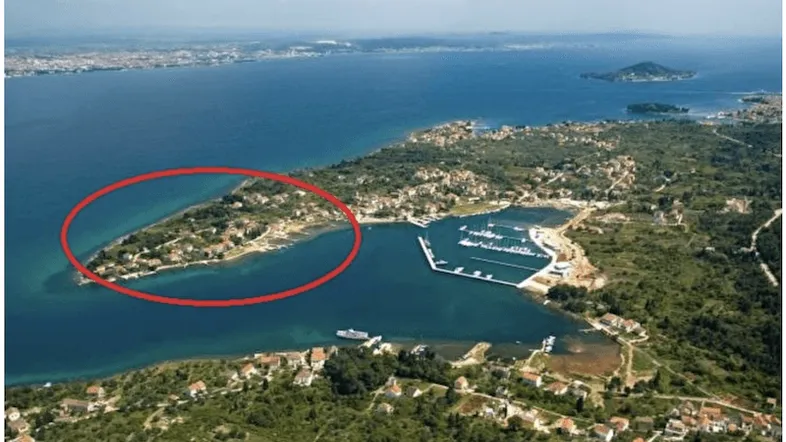 Luftaufnahme einer Küstenlandschaft mit Bucht, Yachthafen und Wohngebieten, umgeben von üppiger Vegetation.