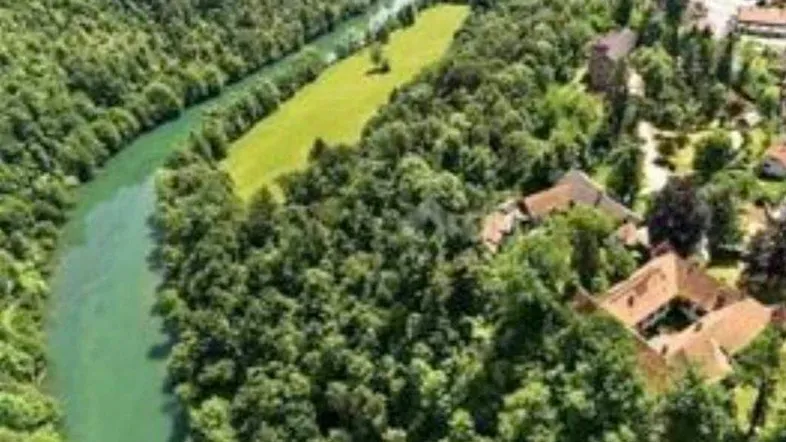 Luftaufnahme einer Flusslandschaft mit dichten Wäldern und vereinzelten Gebäuden in ländlicher Umgebung.