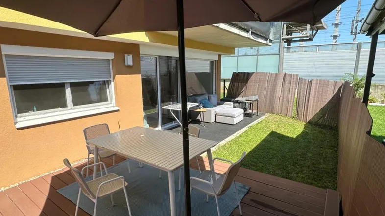 Gemütliche Terrasse mit Holzboden, Esstisch und Sonnenschirm, angrenzend an einen kleinen Gartenbereich.