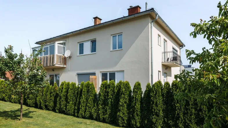 Außenansicht eines Einfamilienhauses mit gepflegtem Garten, Hecke und kleinem Balkon.
