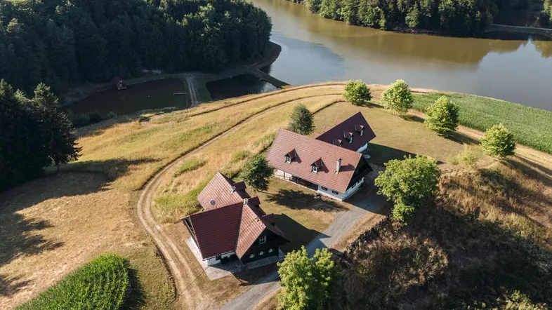 Luftaufnahme von zwei Häusern in ländlicher Umgebung mit See und Wald.