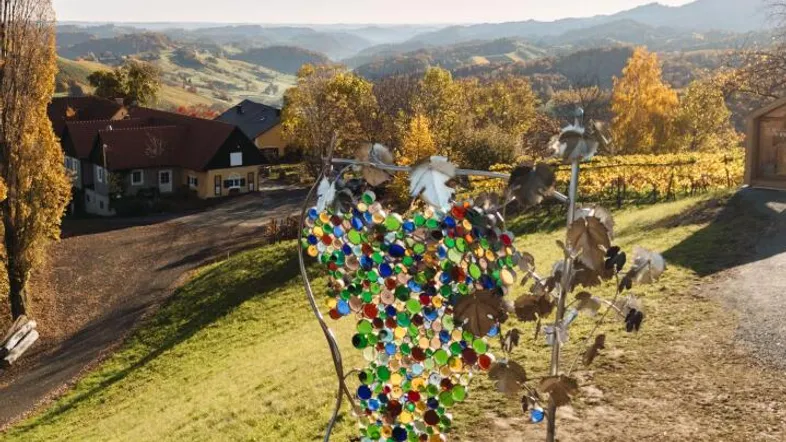 Kunstinstallation in Form einer Weintraube mit bunten Glasstücken vor einer malerischen Weinlandschaft.