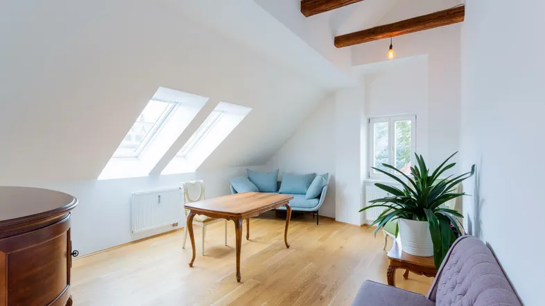 Heller Wohnbereich im Dachgeschoss mit sichtbaren Holzbalken, Dachfenstern und Parkettboden.