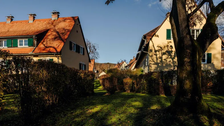 Traditionelle Häuser mit roten Ziegeldächern und grünen Fensterläden, eingebettet in eine grüne Umgebung.