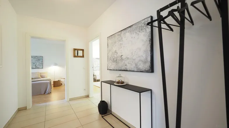 Heller Flur mit Fliesenboden und modernem Konsolentisch, der zum Schlafzimmer führt.