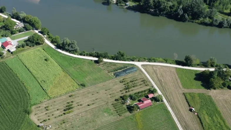Luftaufnahme eines Flusses, umgeben von landwirtschaftlichen Feldern und kleinen Gebäuden mit roten Dächern.