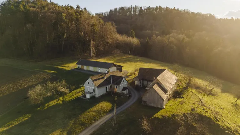 Luftaufnahme eines Anwesens mit mehreren Gebäuden, umgeben von grünen Hügeln und Wald bei Sonnenuntergang.