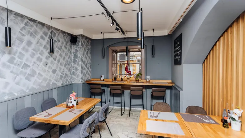 Gemütlicher Restaurantbereich mit Holztischen, Barhockern und moderner Beleuchtung, die eine einladende Atmosphäre schafft.