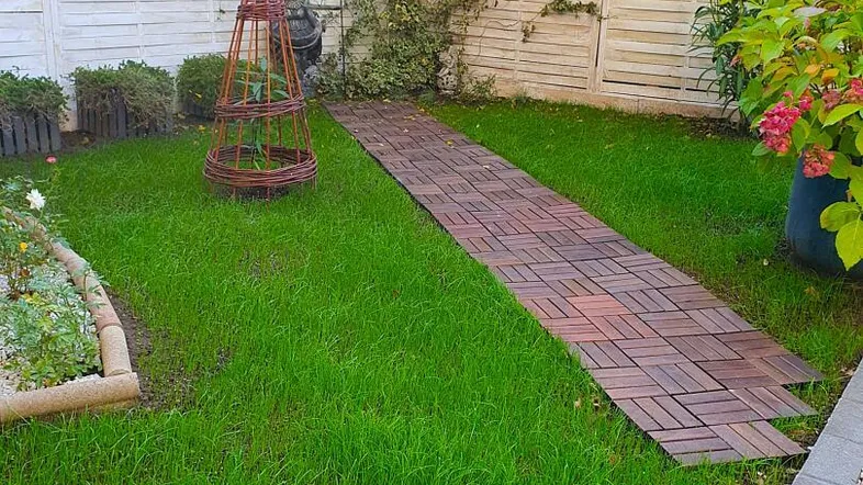Gepflegter Gartenbereich mit Rasenfläche, Holzwegen und einem hohen Sichtschutzzaun.