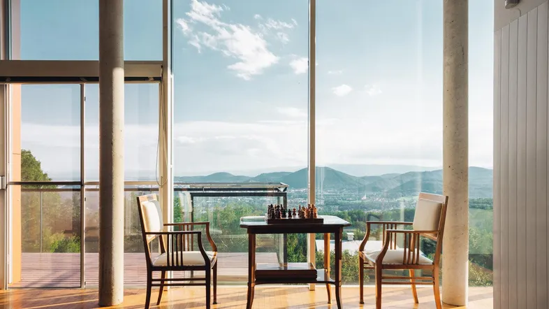 Helles Wohnzimmer mit Holzboden, Schachspiel und weitem Blick auf die Landschaft und Berge.