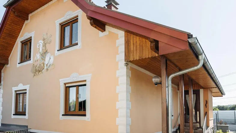 Traditionelle Hausfassade mit dekorativen Elementen und gepflegtem Vorgarten unter blauem Himmel.