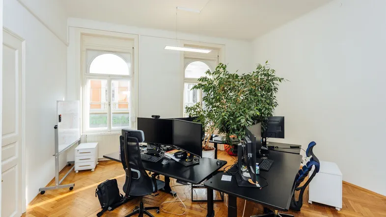 Geräumiges Büro mit mehreren Arbeitsplätzen, großen Fenstern und einem schönen Fischgrätparkettboden.