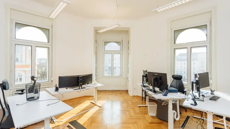 Helles Büro mit Fischgrätparkett, großen Fenstern und modernen Arbeitsplätzen.