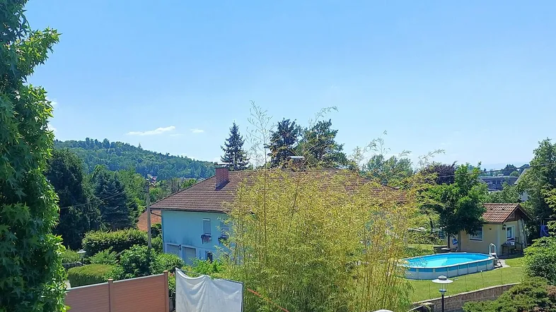 Blick über die Nachbarschaft mit Häusern, Bäumen und einem Pool im Garten. Hügel sind in der Ferne sichtbar.