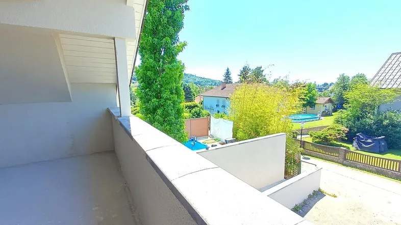 Leerer Balkon mit Blick auf die Straße und die grüne Umgebung mit Häusern und Bäumen.