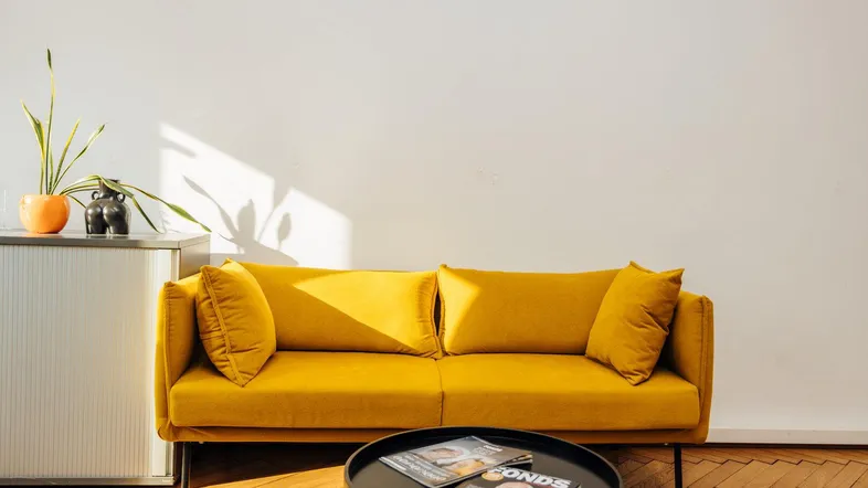 Gemütlicher Wartebereich mit einem leuchtend gelben Sofa und einem runden Couchtisch, beleuchtet von natürlichem Licht.