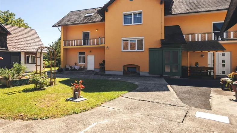 Gelbes Wohnhaus mit Balkonen, umgeben von einem gepflegten Garten und einer Einfahrt.