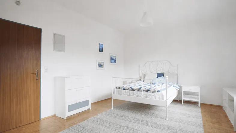 Helles Schlafzimmer mit weißem Metallbett, Parkettboden und schlichten Möbeln, ideal für eine ruhige Atmosphäre.