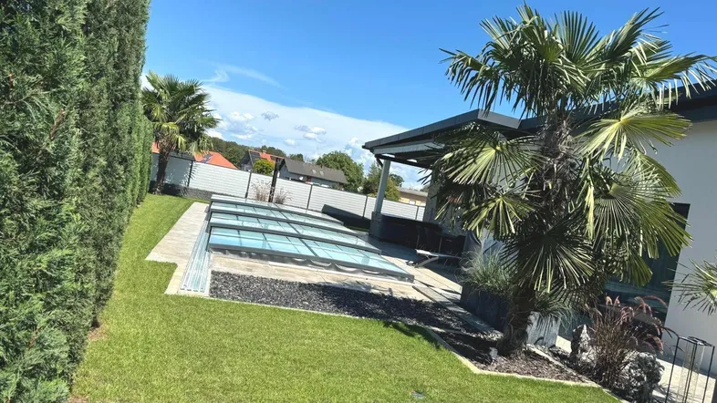 Gepflegter Gartenbereich mit Rasenfläche, Palmen und einem modernen Pool mit Abdeckung.