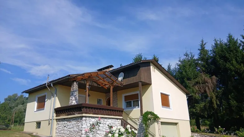 Gesamtansicht des Einfamilienhauses mit Garten und umgebender Natur unter blauem Himmel.