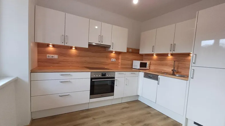 Moderne Einbauküche mit weißen Hochglanzfronten, Holzoptik-Arbeitsplatte und Laminatboden.