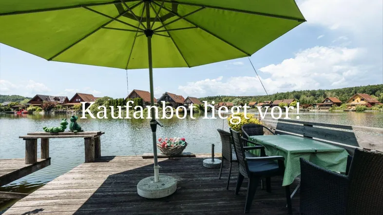 Gemütliche Terrasse am Seeufer mit Sonnenschirm und Sitzgelegenheiten, ideal zum Entspannen.